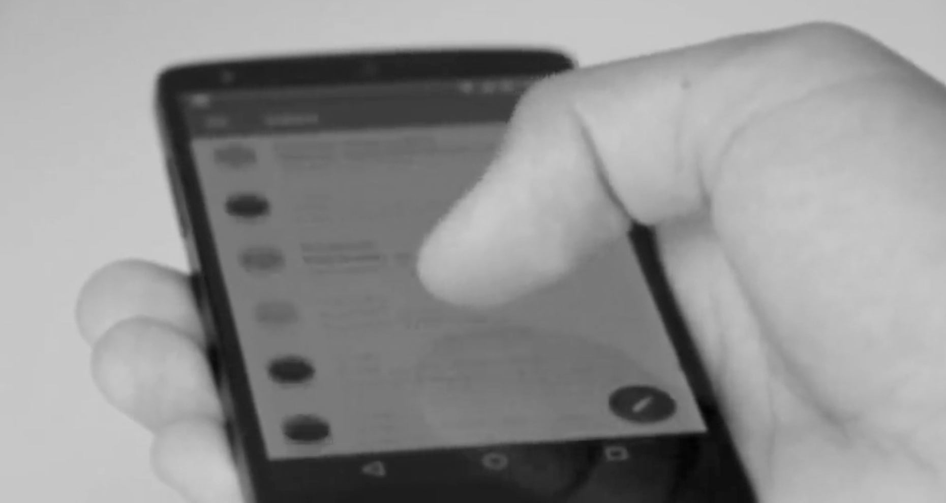 A black and white closeup image of a hand holding and scrolling through a smartphone