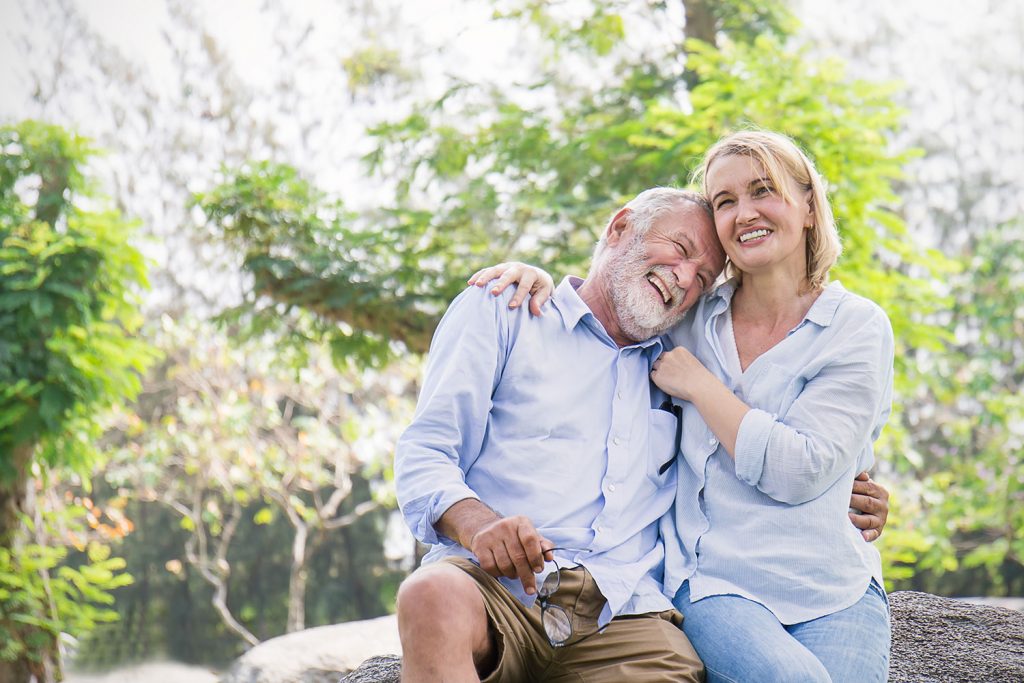 Happy older couple sitting together with their arms around each other.