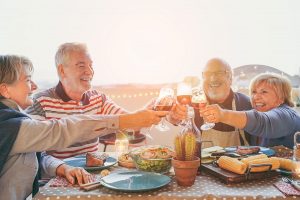 Happy older couples cheers with wine glasses at dinner